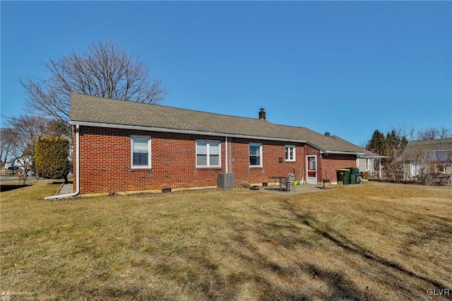 back of property featuring central AC unit, brick siding, roof with shingles, a lawn, and a chimney