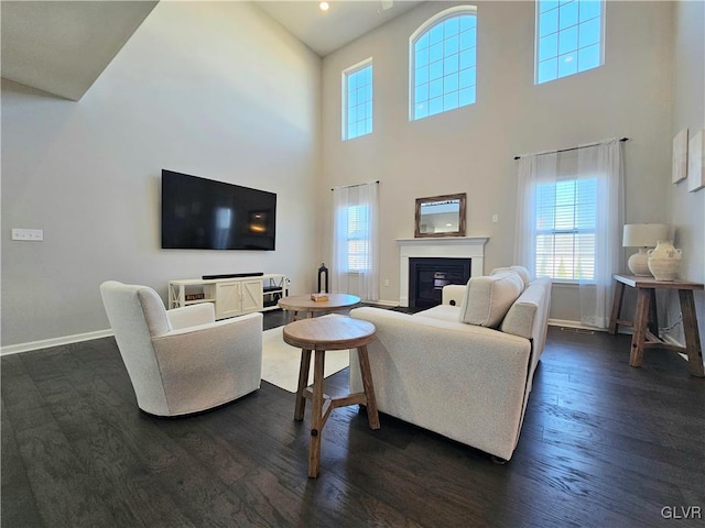 living area featuring dark wood-style floors, a glass covered fireplace, a healthy amount of sunlight, and baseboards