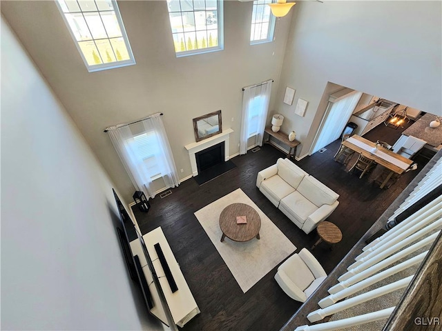 living room featuring a fireplace, wood finished floors, visible vents, a towering ceiling, and baseboards