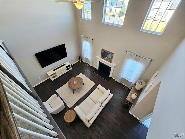 living area with ceiling fan, a high ceiling, a fireplace, baseboards, and dark wood-style floors