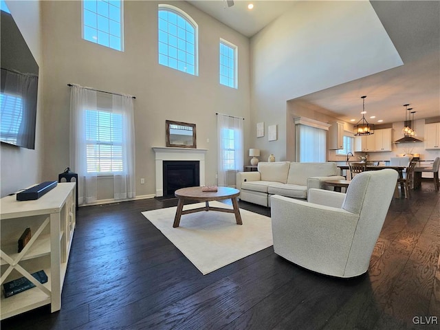 living area featuring a chandelier, recessed lighting, dark wood finished floors, baseboards, and a glass covered fireplace