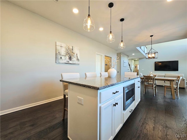 kitchen with dark wood-style floors, stainless steel microwave, a kitchen bar, and white cabinetry