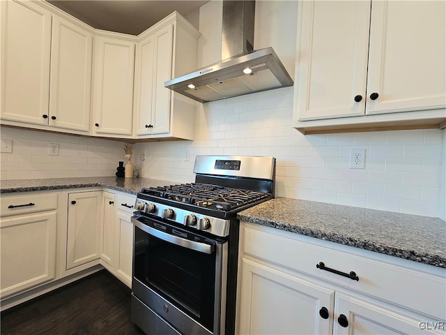 kitchen with wall chimney exhaust hood, decorative backsplash, dark stone countertops, and stainless steel gas range oven