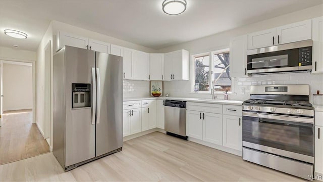 kitchen with stainless steel appliances, light countertops, white cabinetry, and a sink