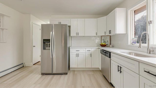 kitchen featuring white cabinets, appliances with stainless steel finishes, baseboard heating, light countertops, and a sink