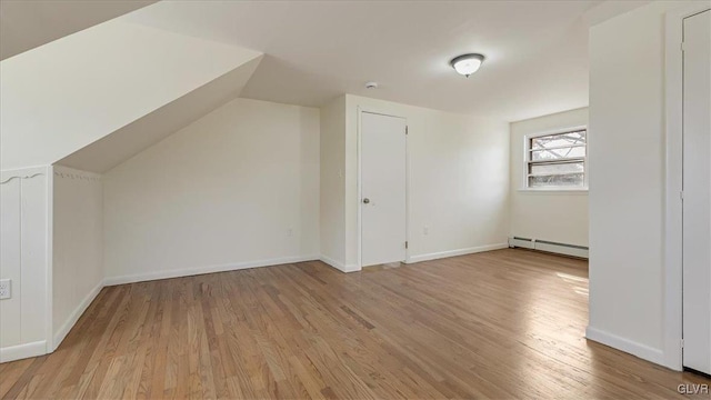 additional living space featuring lofted ceiling, baseboard heating, light wood-style flooring, and baseboards