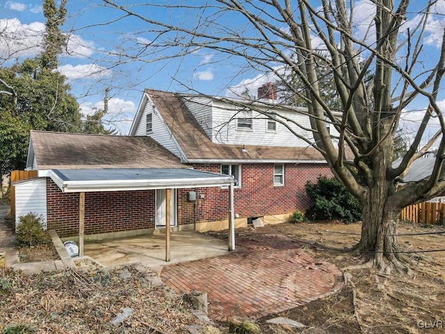 view of property exterior with brick siding, fence, roof with shingles, a chimney, and a patio area