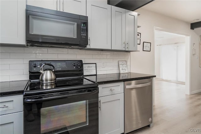 kitchen with decorative backsplash, dark stone counters, light wood-style flooring, and black appliances