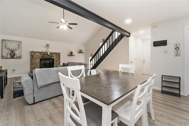 dining area with vaulted ceiling with beams, light wood-style floors, stairway, and a stone fireplace