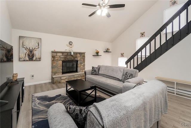 living area with a stone fireplace, wood finished floors, a ceiling fan, stairs, and vaulted ceiling