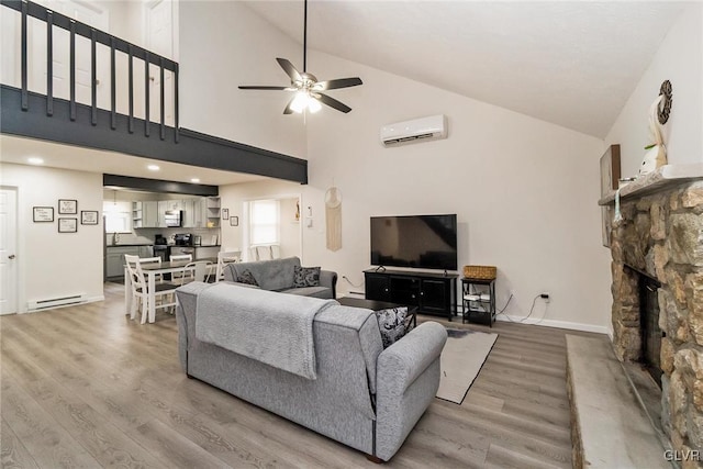 living room with a ceiling fan, baseboard heating, an AC wall unit, a stone fireplace, and light wood-type flooring