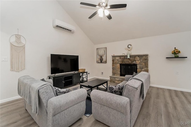 living area with a stone fireplace, a wall mounted AC, wood finished floors, and baseboards