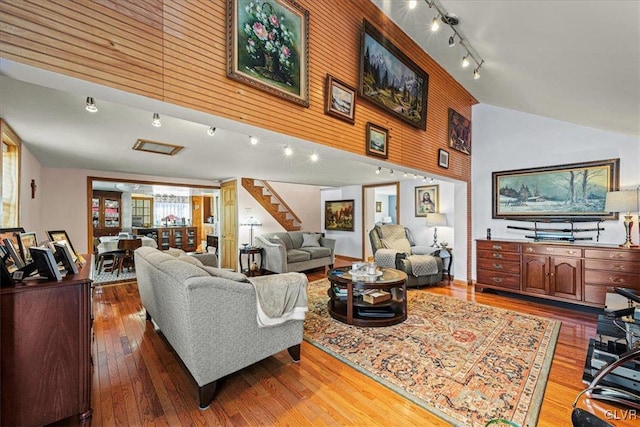 living area featuring high vaulted ceiling, stairway, rail lighting, and hardwood / wood-style flooring