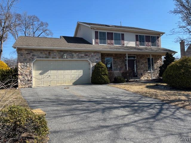 traditional home with driveway, stone siding, covered porch, an attached garage, and solar panels