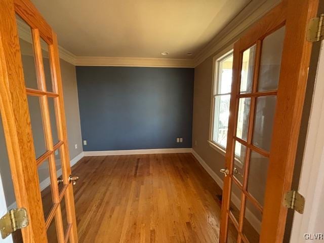 empty room with french doors, baseboards, wood finished floors, and crown molding