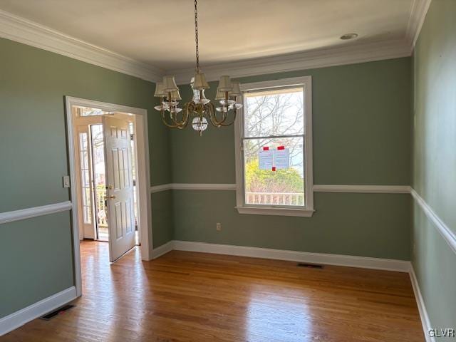 unfurnished dining area with visible vents, crown molding, baseboards, an inviting chandelier, and wood finished floors