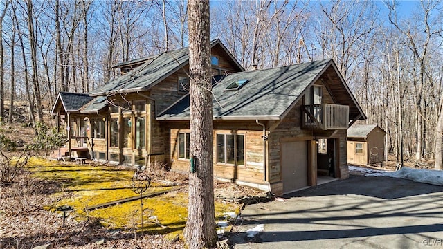 chalet / cabin with a sunroom, aphalt driveway, a shingled roof, and a balcony