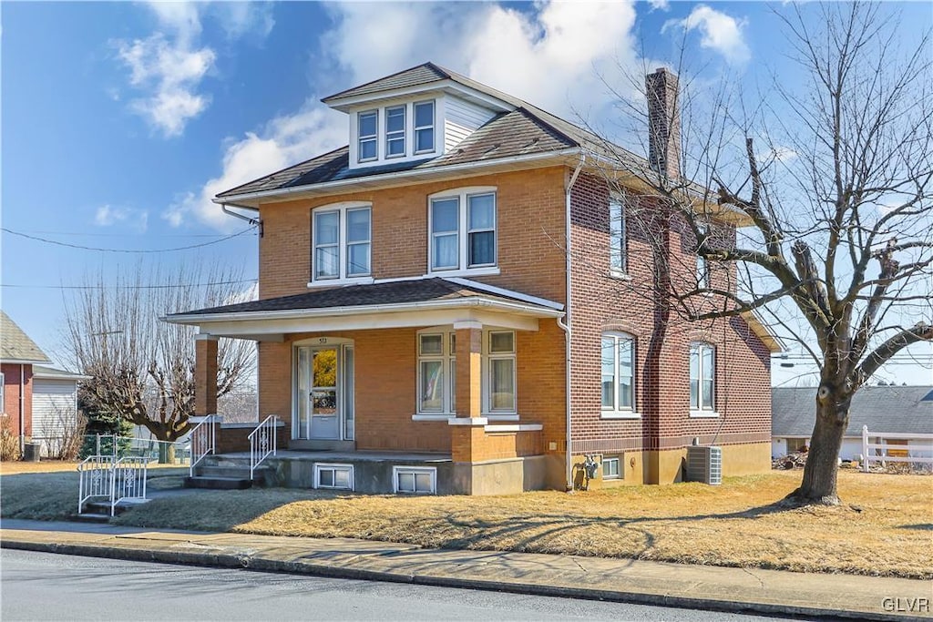 american foursquare style home featuring brick siding, a chimney, a porch, and central air condition unit