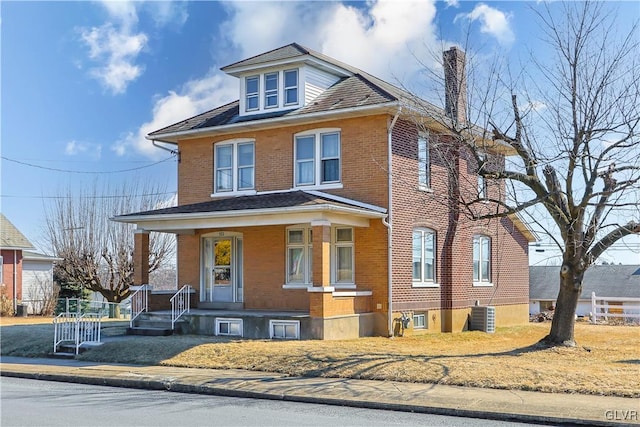 american foursquare style home featuring brick siding, a chimney, a porch, and central air condition unit