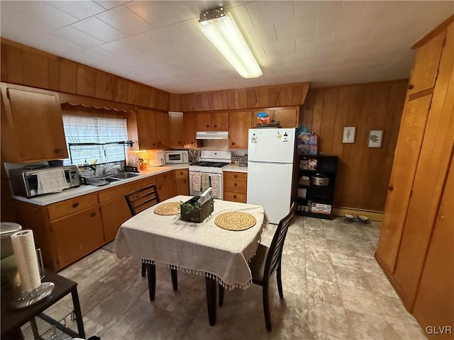 kitchen featuring under cabinet range hood, white appliances, wood walls, a sink, and brown cabinets