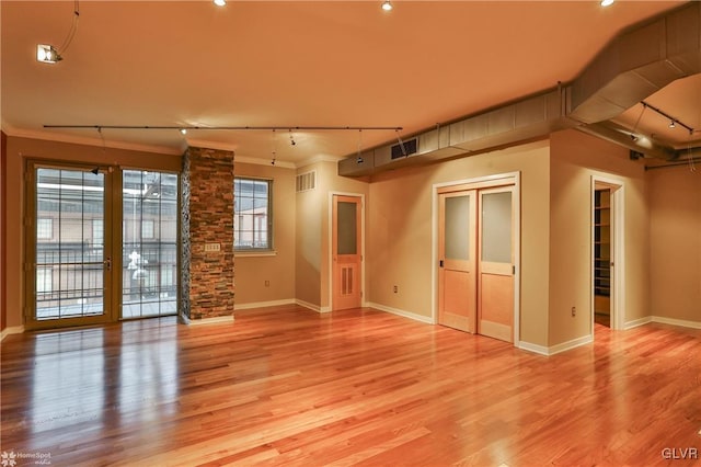 empty room with visible vents, baseboards, ornamental molding, light wood-type flooring, and rail lighting