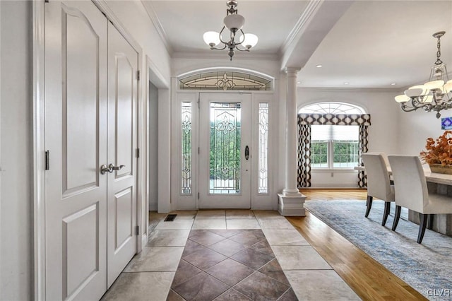 foyer with crown molding, decorative columns, and an inviting chandelier