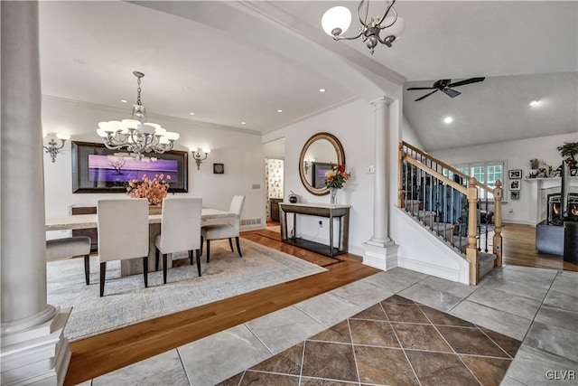 tiled dining area featuring ceiling fan with notable chandelier, ornamental molding, vaulted ceiling, ornate columns, and stairs