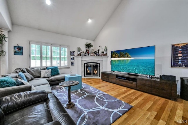 living area with high vaulted ceiling, wood finished floors, and a glass covered fireplace