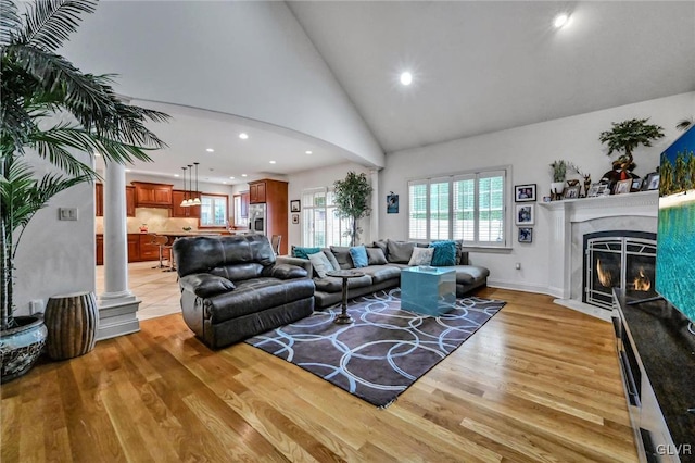 living room featuring light wood-type flooring, plenty of natural light, high vaulted ceiling, and a fireplace with flush hearth