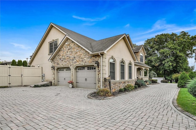 view of property exterior with fence, stone siding, decorative driveway, a gate, and stucco siding