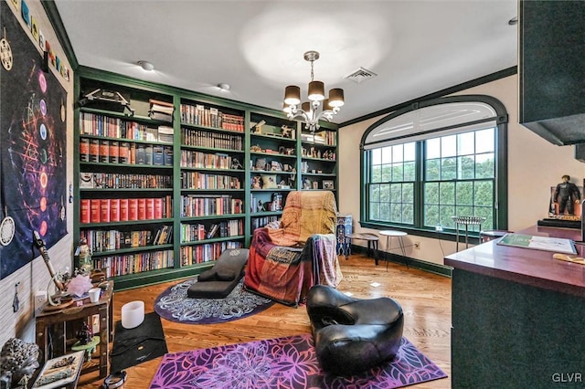 living area featuring ornamental molding, visible vents, a notable chandelier, and wood finished floors