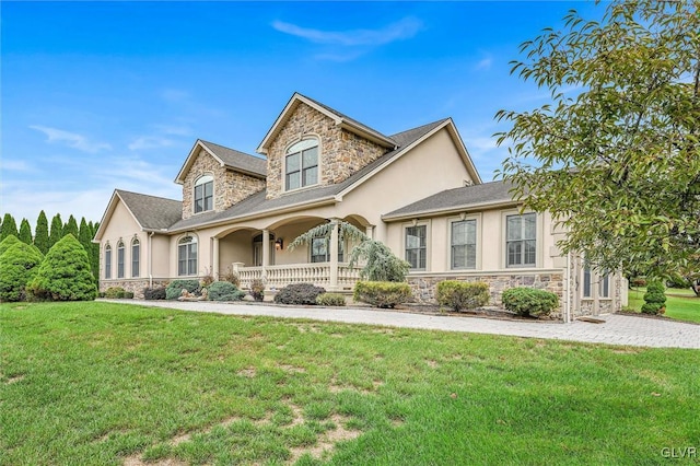 view of front facade with covered porch, stone siding, a front yard, and stucco siding