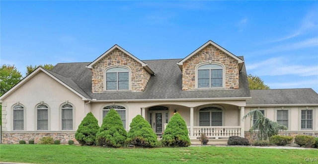 view of front of home with covered porch, roof with shingles, a front yard, and stucco siding