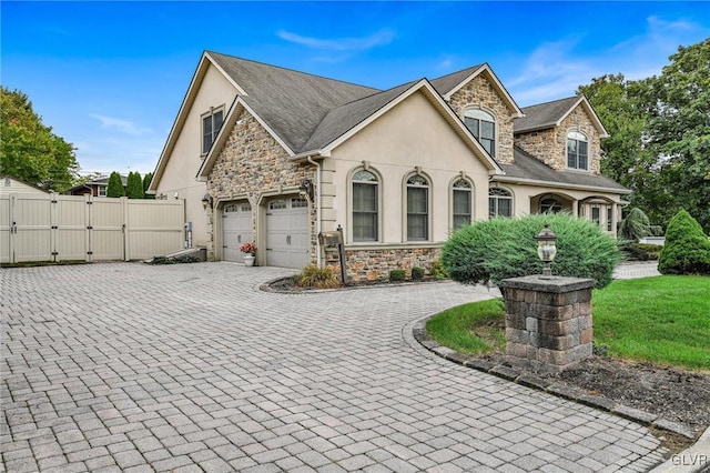 view of front of property with a garage, stone siding, decorative driveway, a gate, and stucco siding