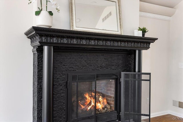 details featuring wood finished floors, baseboards, visible vents, and a warm lit fireplace