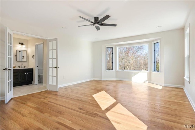 empty room with baseboards, french doors, light wood-type flooring, and a sink