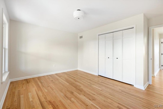 unfurnished bedroom with a closet, visible vents, light wood-type flooring, and baseboards