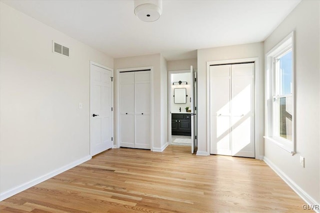 unfurnished bedroom with light wood-type flooring, visible vents, baseboards, and two closets