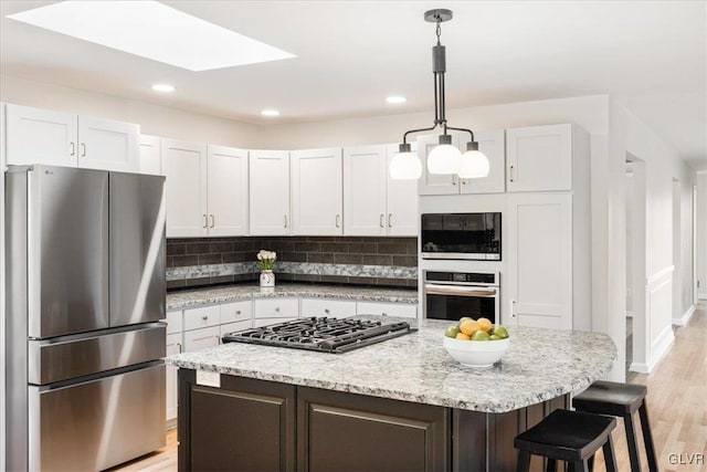 kitchen with a kitchen island, decorative backsplash, light wood-style flooring, appliances with stainless steel finishes, and hanging light fixtures