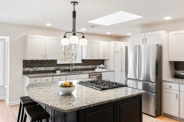 kitchen with visible vents, a kitchen island, a sink, stainless steel appliances, and a kitchen bar