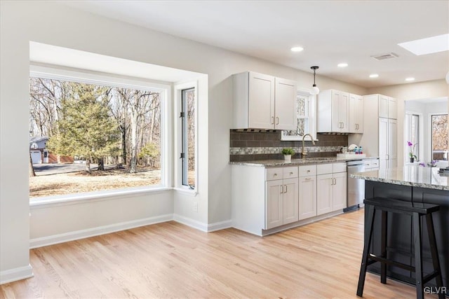 kitchen with tasteful backsplash, visible vents, dishwasher, light stone counters, and a sink