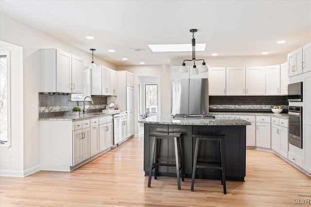 kitchen featuring a kitchen island, stainless steel appliances, a sink, light wood-style floors, and a kitchen bar