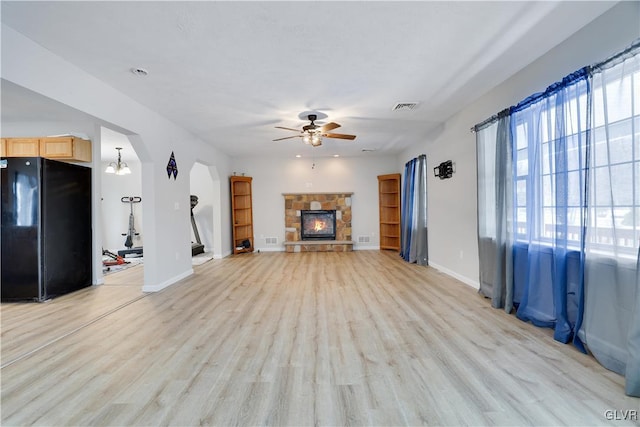 unfurnished living room featuring arched walkways, visible vents, light wood-style flooring, a ceiling fan, and a stone fireplace