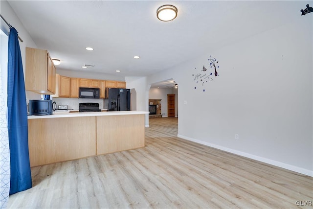 kitchen with light brown cabinetry, light wood-style floors, open floor plan, a peninsula, and black appliances