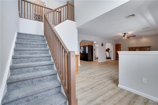 stairway with arched walkways, visible vents, a ceiling fan, wood finished floors, and baseboards