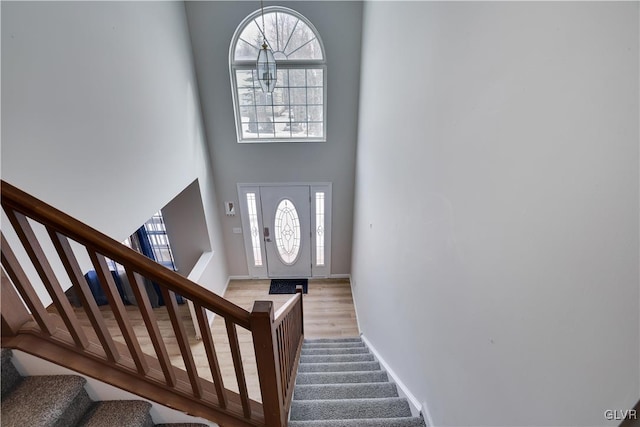 foyer entrance with a towering ceiling, stairs, baseboards, and wood finished floors