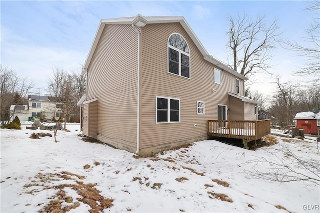 snow covered rear of property featuring a garage and a deck