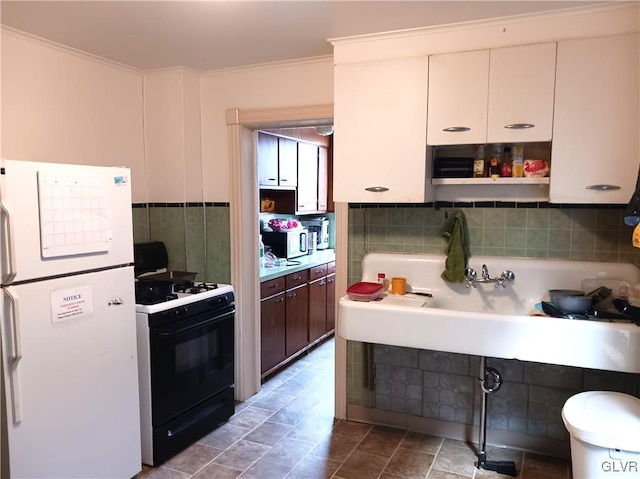 kitchen featuring freestanding refrigerator, light countertops, crown molding, white cabinetry, and gas stove