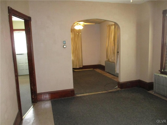 empty room with arched walkways, radiator heating unit, baseboards, and radiator