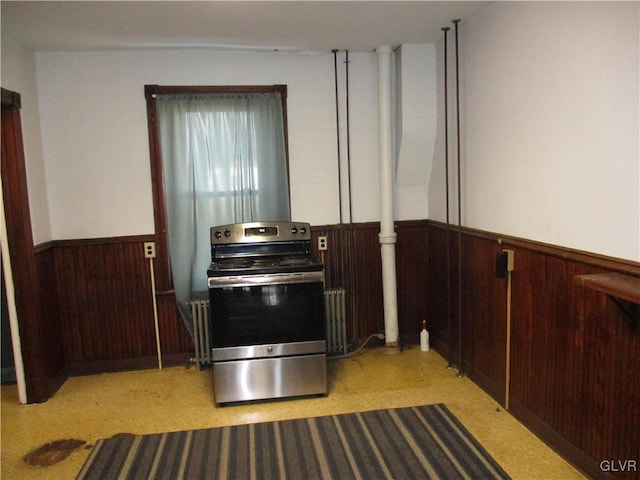 kitchen with a wainscoted wall, electric range, radiator heating unit, and wood walls